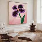A modern living room with a white leather lounge chair and ottoman, dark wood side table with a white lamp, and the Purple Pansy Canvas Art - Square featuring a large botanical print on a pink background.