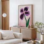 A modern living room with a white sofa, light wood sideboard, and the Purple Pansy Canvas Art - Vertical on the wall. Neutral decor, books, ceramic vases, and a small green plant complete this Nordic Park-inspired space.