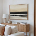 A light, modern living room features a wooden sideboard with books, a lamp, and decor bowl. Above hangs the Quiet Shoreline Canvas Art - Horizontal in serene neutral tones. A white sofa sits in this calming space.