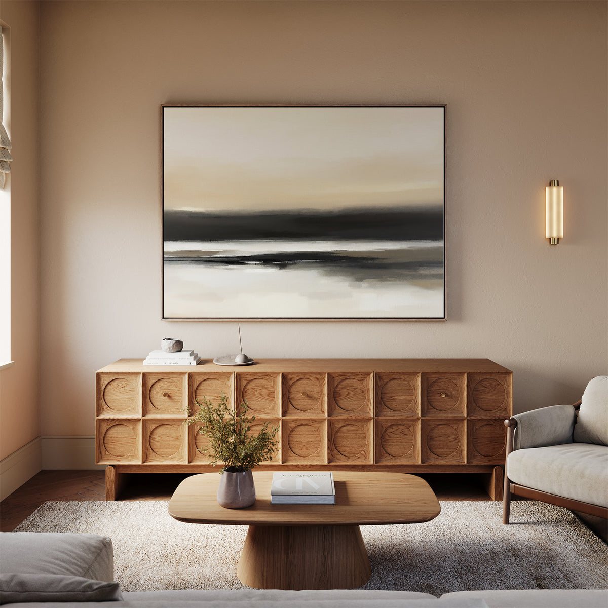 A modern living room with neutral decor features a wooden sideboard, the Quiet Shoreline Canvas Art - Horizontal, a coffee table with books, a beige rug, and a light sofa. Warm lighting and minimal accessories create a cozy, tranquil atmosphere.