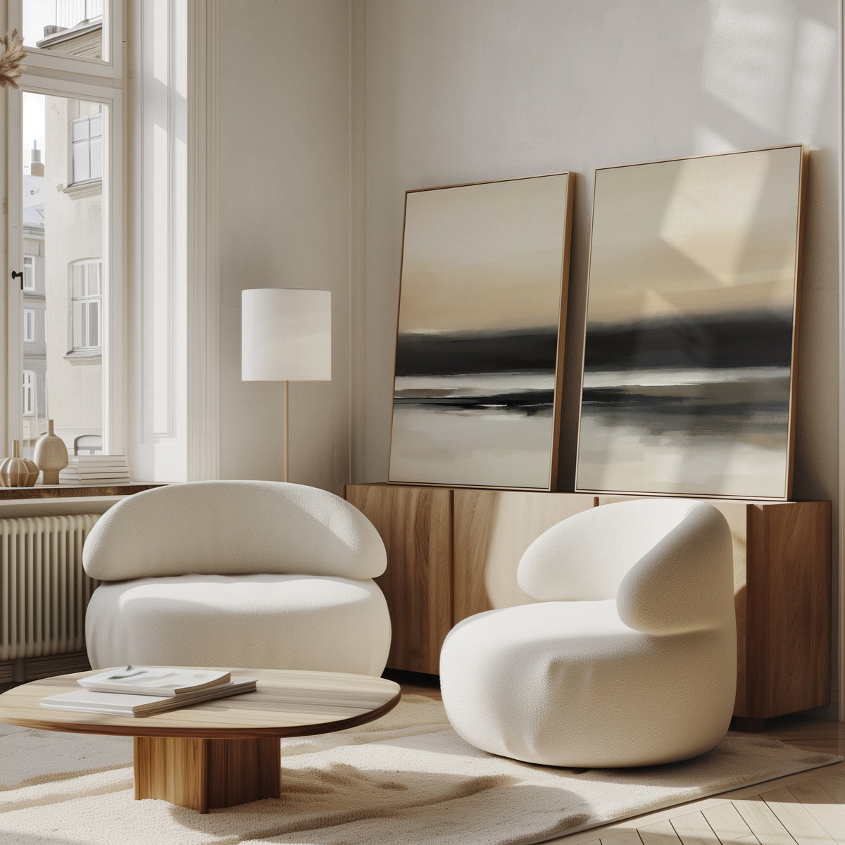 Two modern white armchairs and a low wooden table furnish a bright living room with large windows. The Quiet Shoreline - Set Of 2 abstract coastal wall art rests on a wooden sideboard, sunlight streaming into the cozy minimalist space.