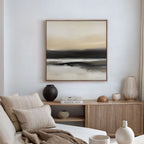 A minimalist living room features the Quiet Shoreline Canvas Art - Square above a wooden sideboard with vases, books, and ceramics. A beige sofa with pillows sits in the foreground, completing the refined minimalist decor.