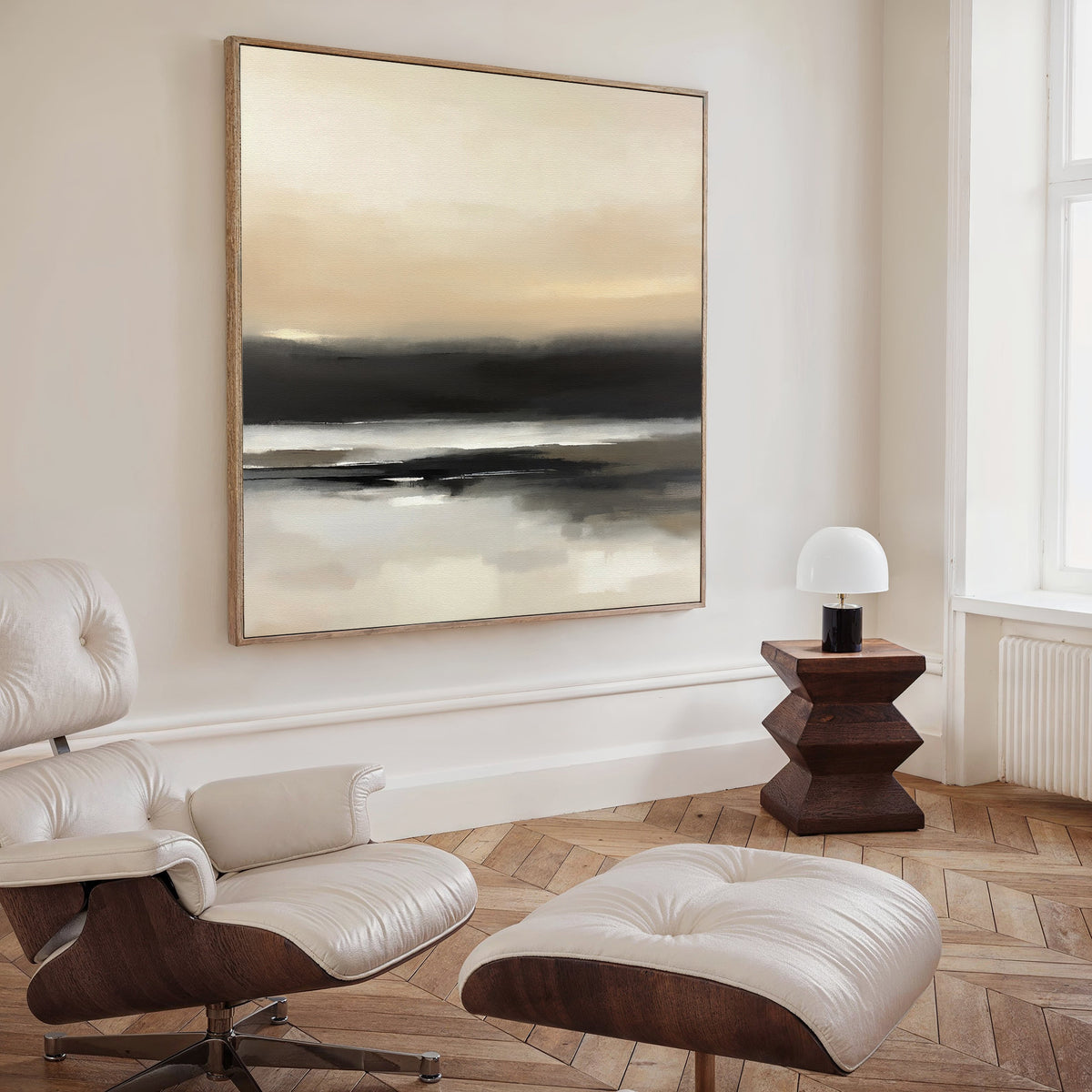 A modern, minimalist living room featuring a white leather lounge chair and ottoman, a geometric wooden side table with a small white lamp, and the Quiet Shoreline Canvas Art - Square in neutral tones displayed above.