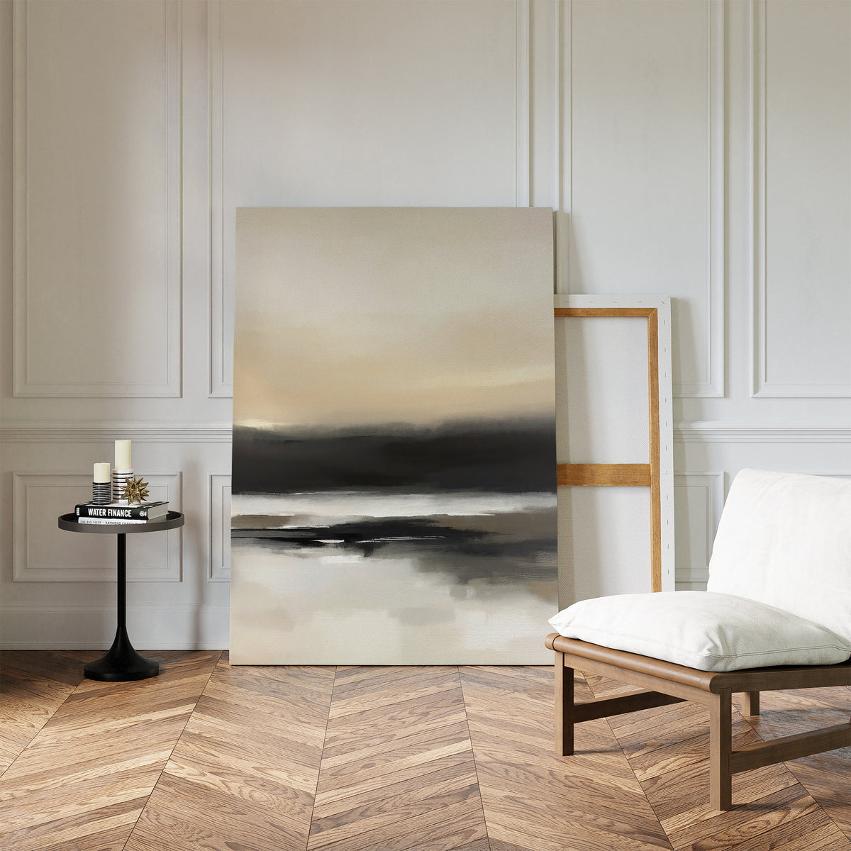 A minimalist room with herringbone wood flooring features the Quiet Shoreline Canvas Art - Vertical leaning against a paneled white wall, next to a cushioned chair and a small round table with candles and books.