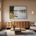 A serene living room features a light wooden sideboard with the River Tranquil Canvas Art - Horizontal above it, a coffee table holding a vase and book, a beige sofa, soft rug, and warm lighting from a wall sconce.