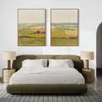 A modern bedroom features a green upholstered bed, white bedding, beige nightstands with matching lamps, and "Rolling Fields - Set of 2" wall art above the bed, showcasing tranquil pastoral countryside scenes in elegant frames.