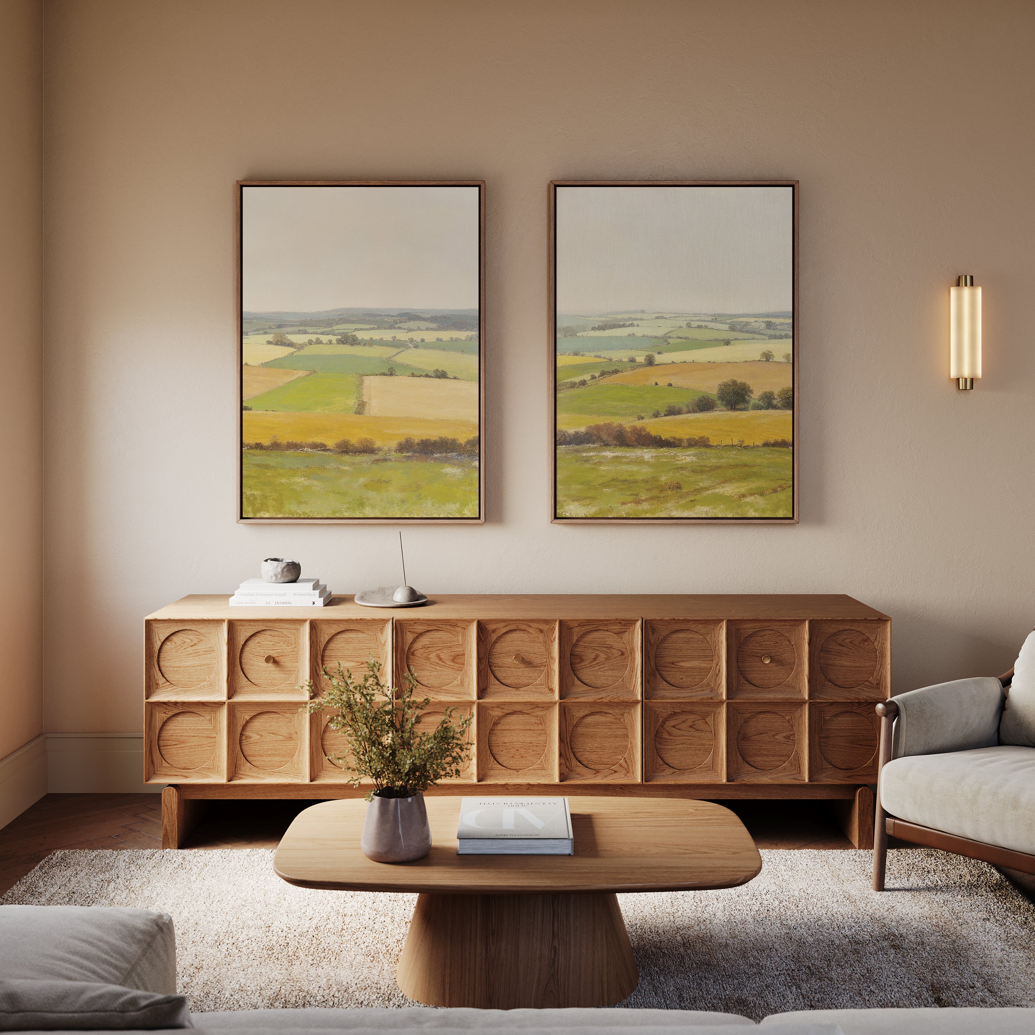 A cozy living room with a wooden coffee table, patterned sideboard, gray sofa, rug, and Rolling Fields - Set of 2 canvas prints of pastoral countryside hanging above the sideboard on a beige wall.