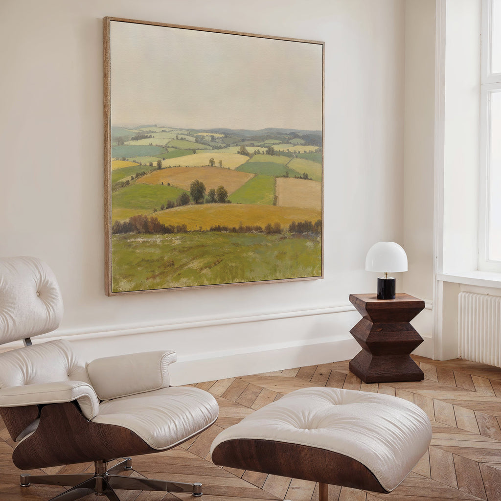 A modern living room features a white leather lounge chair and ottoman, a wooden side table with a white lamp, and serene decor with the Rolling Fields Canvas Art - Square, creating a tranquil, inviting atmosphere.