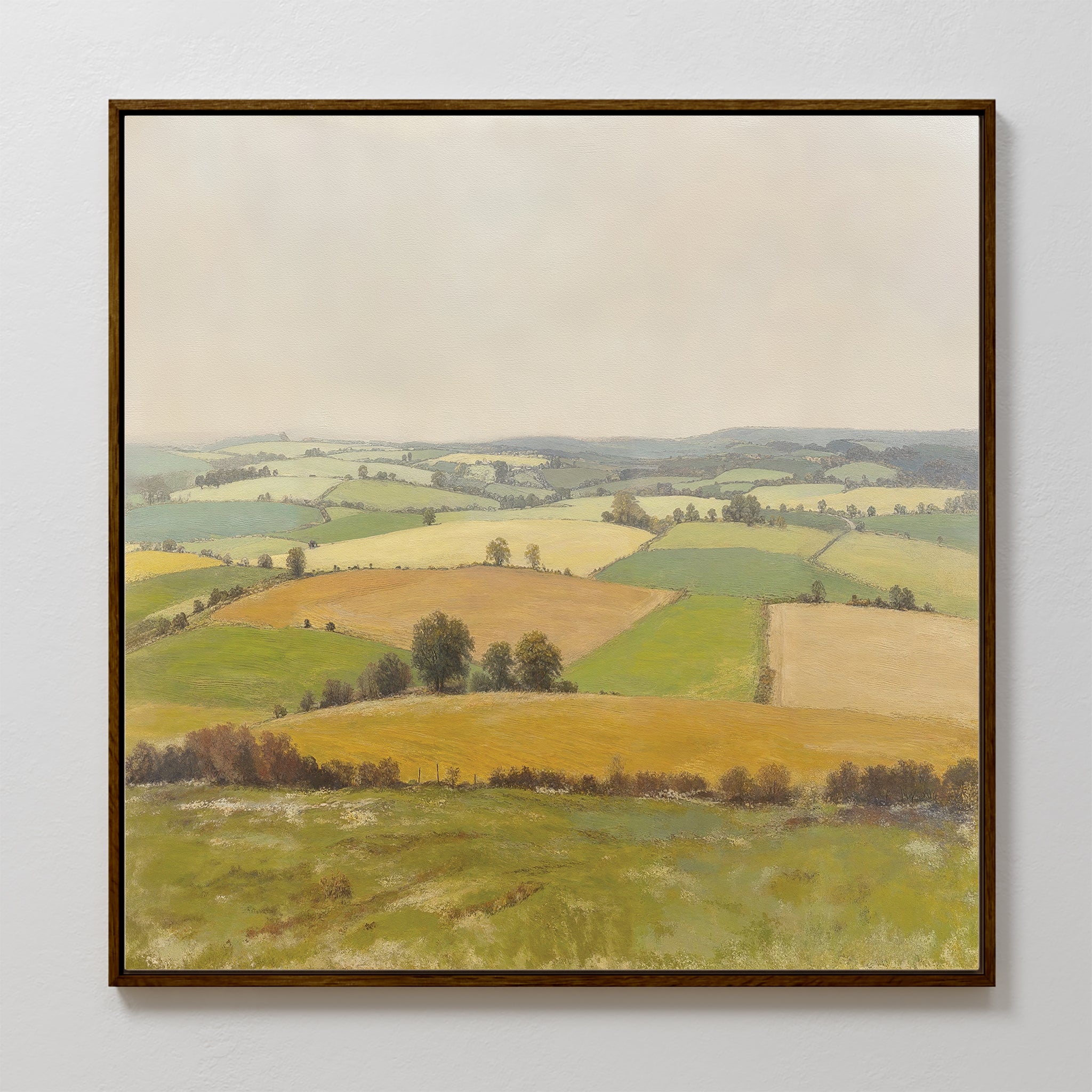 Rolling Fields Canvas Art - Square: This framed canvas print features serene rolling hills and patchwork fields in green and yellow beneath a pale, cloudy sky, with hedgerows and scattered trees completing the tranquil landscape.