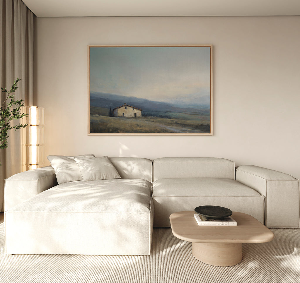 Minimalist living room featuring a light beige sectional sofa, wooden coffee table, and the Rustic Solitude Canvas Art - Horizontal—a large landscape painting. Neutral tones and soft natural light create a calm, inviting atmosphere.