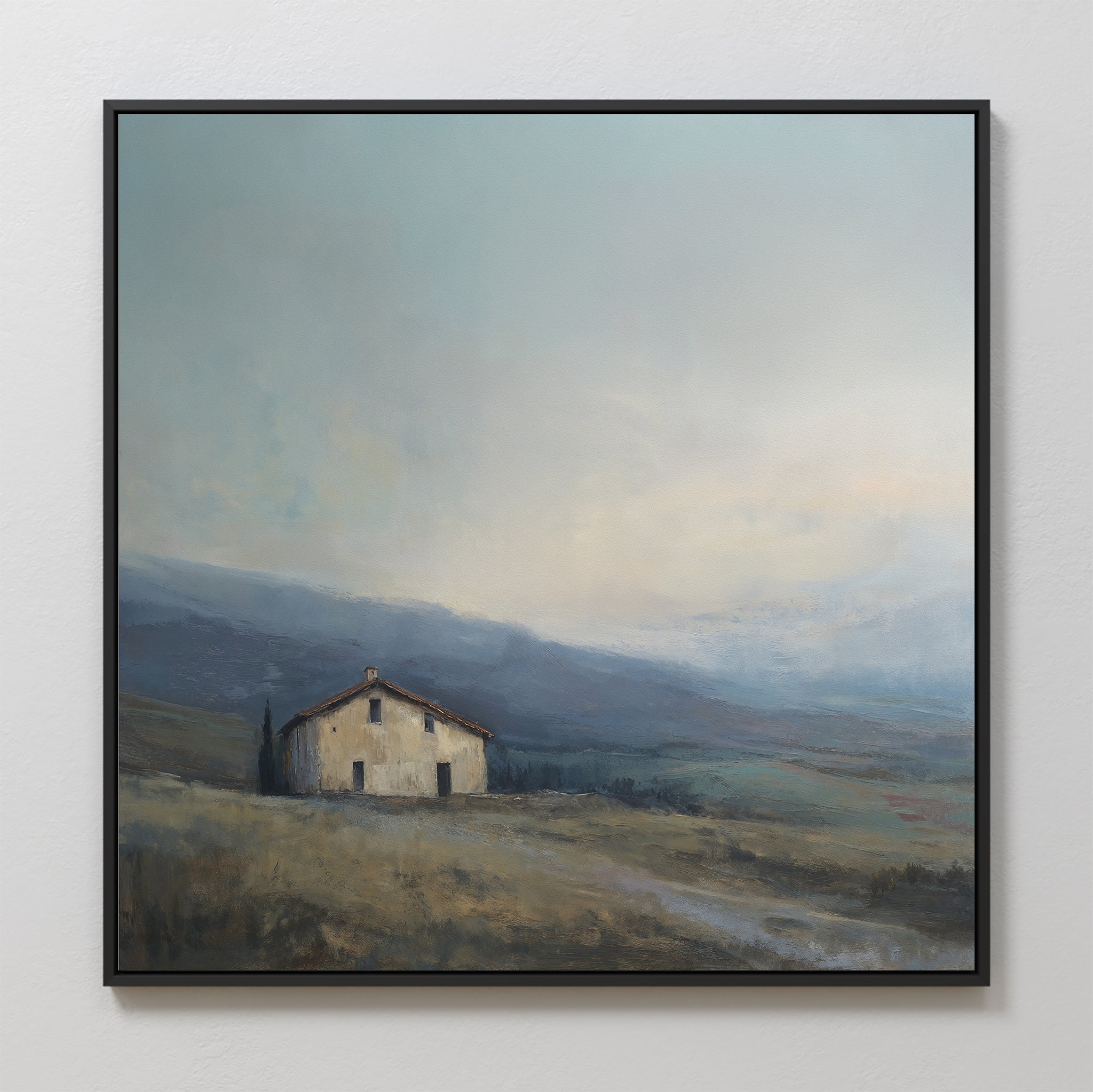The Rustic Solitude Canvas Art - Square features a small house on a grassy hillside beneath a cloudy sky, framed by rolling hills and distant mountains—ideal farmhouse wall art for serene landscape decor.