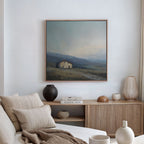 A minimal, neutral-toned living room features a beige sofa with striped pillows, a wooden sideboard with vases and books, and the Rustic Solitude Canvas Art - Square displayed above the mantel.