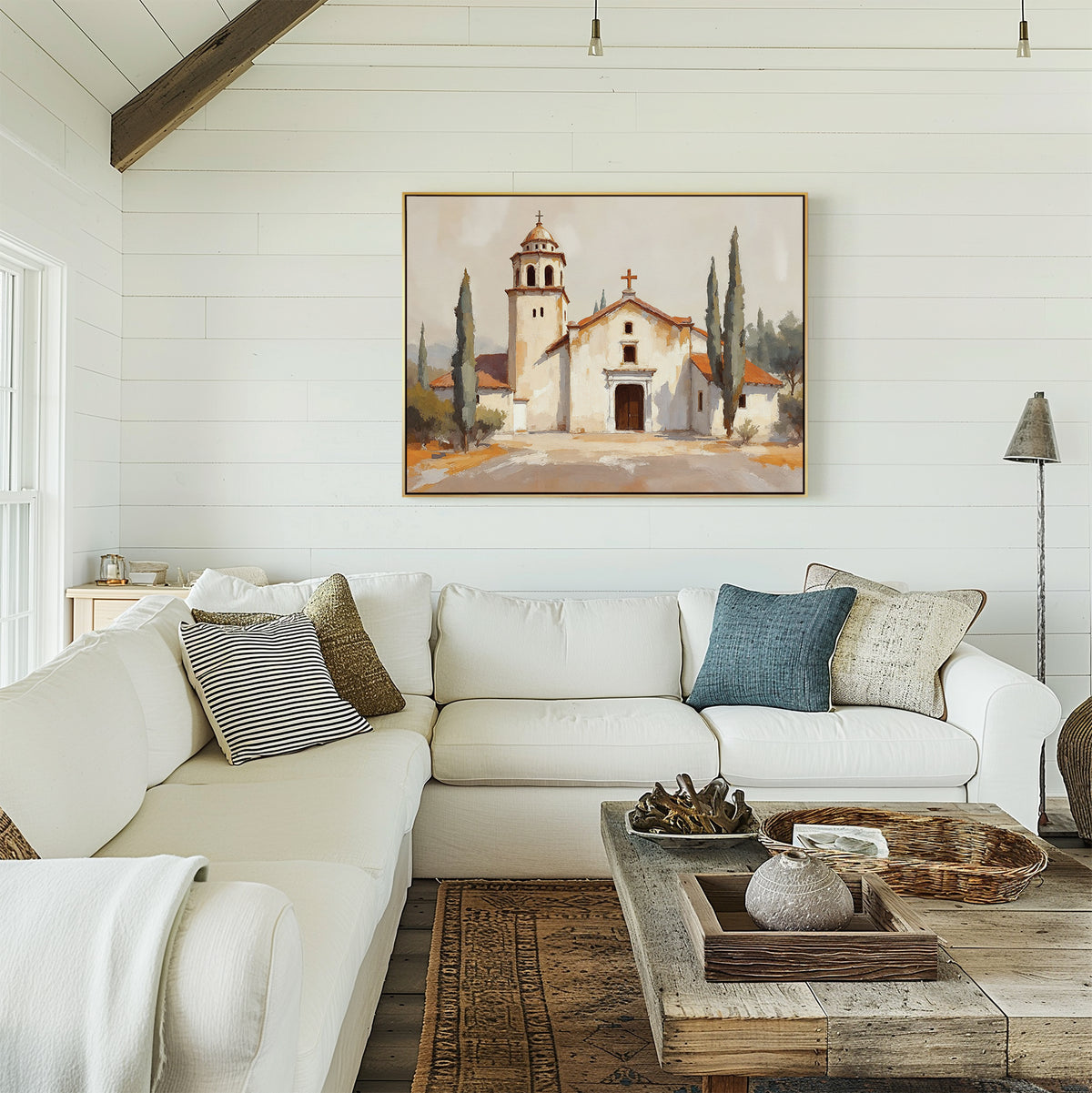 Bright, cozy living room with a white sectional, neutral and patterned pillows, rustic wood coffee table, and the Sacred Courtyard Canvas Art - Horizontal featuring a Spanish colonial church and cypress trees on a white shiplap wall.
