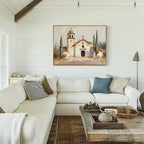 Bright, cozy living room with a white sectional, neutral and patterned pillows, rustic wood coffee table, and the Sacred Courtyard Canvas Art - Horizontal featuring a Spanish colonial church and cypress trees on a white shiplap wall.