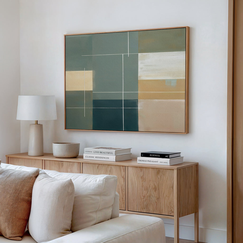 A modern living room features a light wood sideboard with a white table lamp, stacked books, and a beige bowl. Above hangs the Sage Compartments Canvas Art - Horizontal in an abstract print. A cream sofa sits in the foreground.