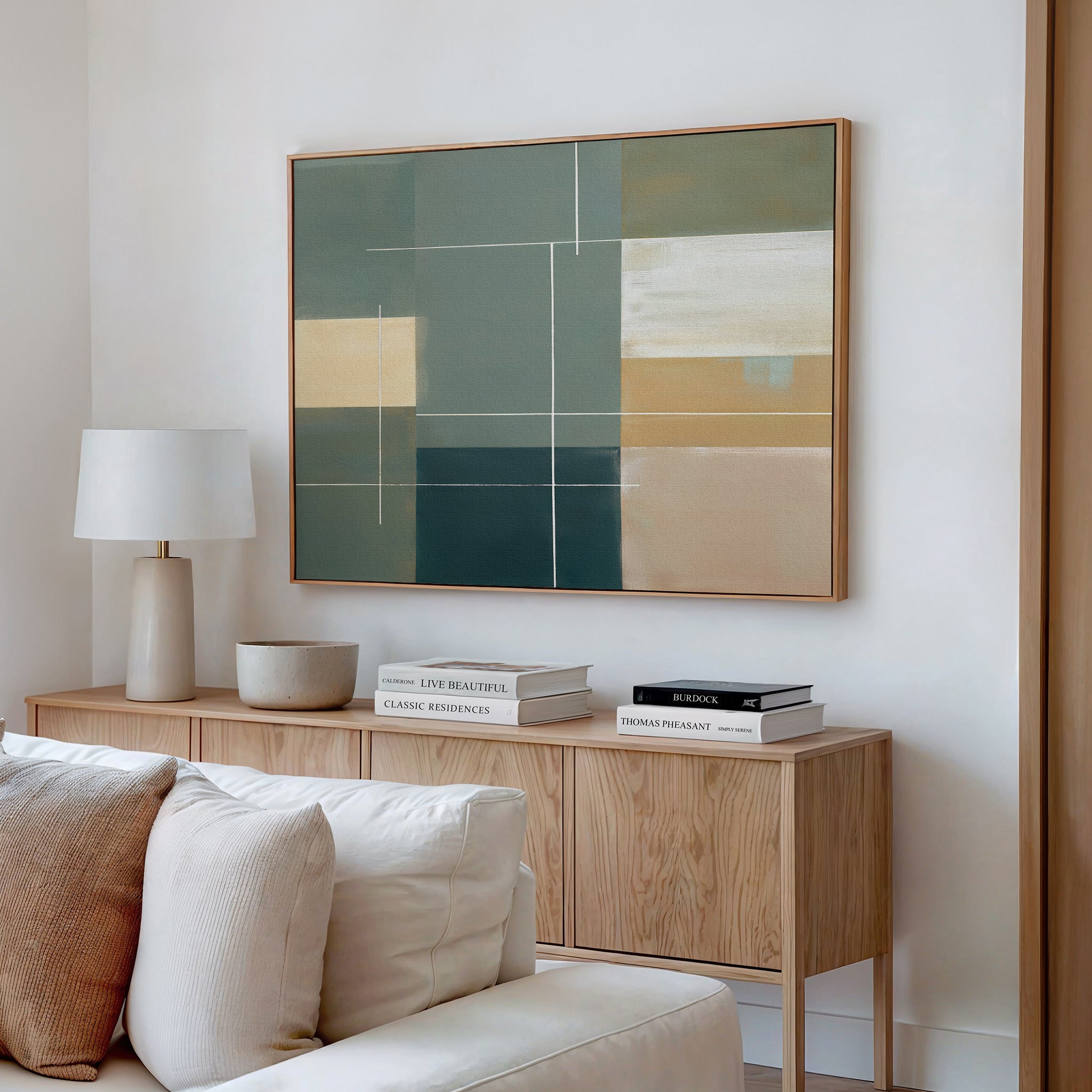 A modern living room features a light wood sideboard with a white table lamp, stacked books, and a beige bowl. Above hangs the Sage Compartments Canvas Art - Horizontal in an abstract print. A cream sofa sits in the foreground.