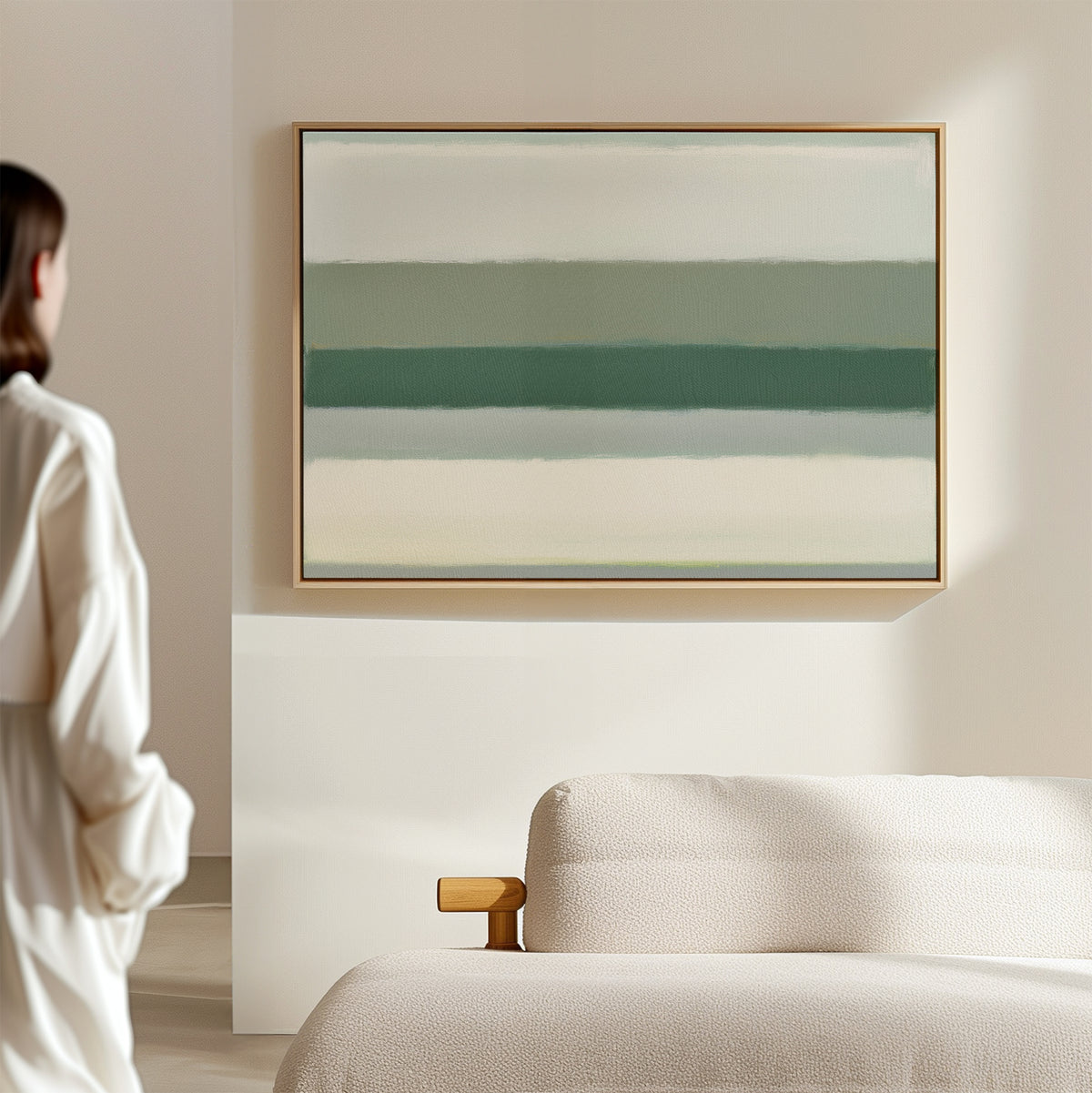 A person stands in a minimalist room, gazing at the Sage Gradient Canvas Art - Horizontal, a large abstract print with soft sage and white stripes, hanging above a light-colored sofa.