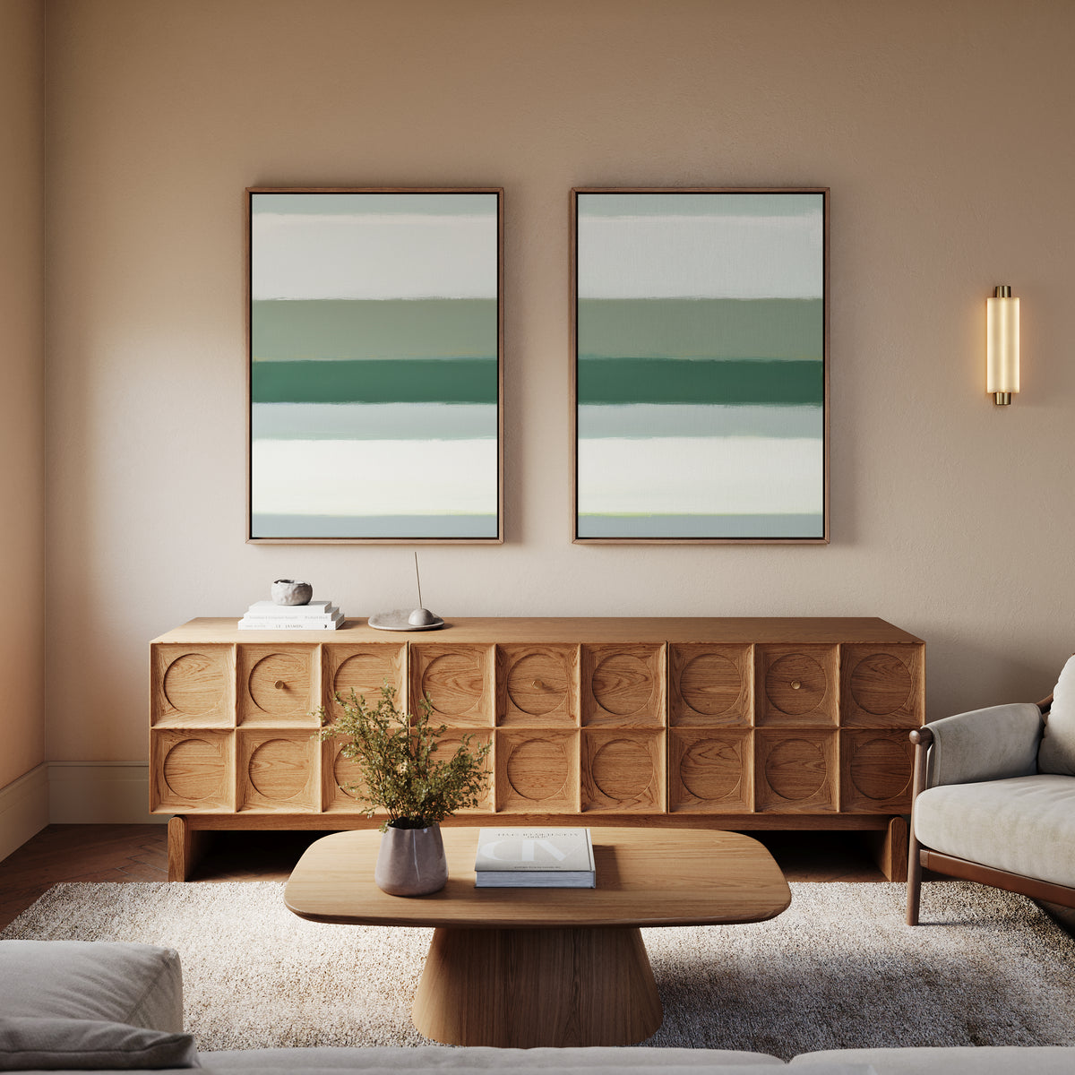 A modern living room features a wooden sideboard with geometric patterns, a low coffee table, a light armchair, the Sage Gradient - Set Of 2 artworks on the wall, and a wall sconce, all in neutral and green tones.