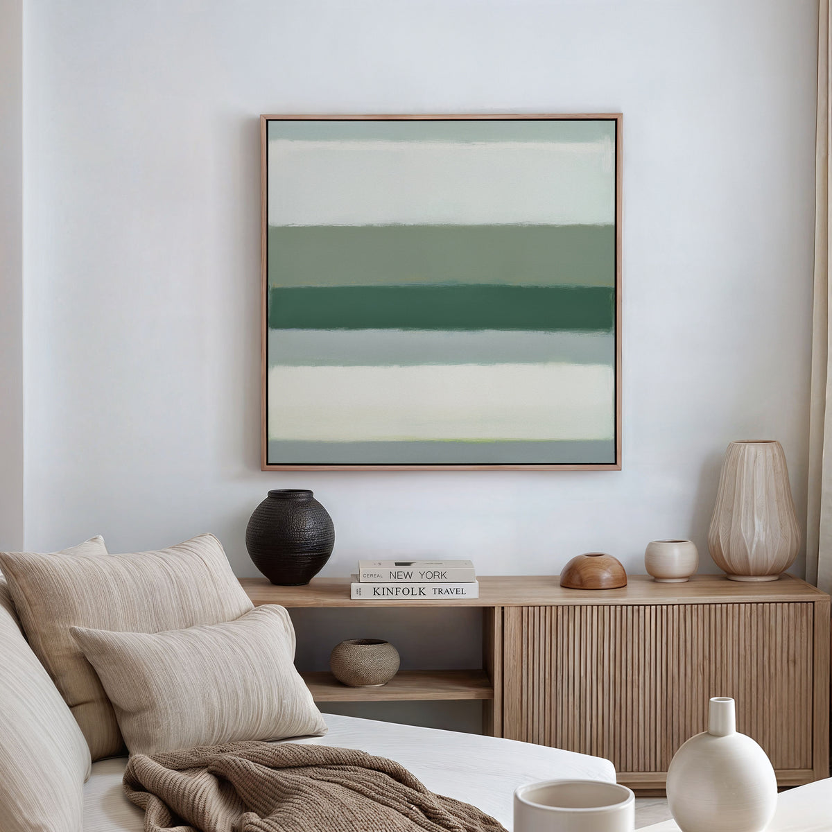 A neutral-toned living room with a beige sofa, textured cushions, a wooden sideboard, decorative vases, books, and the Sage Gradient Canvas Art - Square featuring green and white horizontal stripes on the wall.