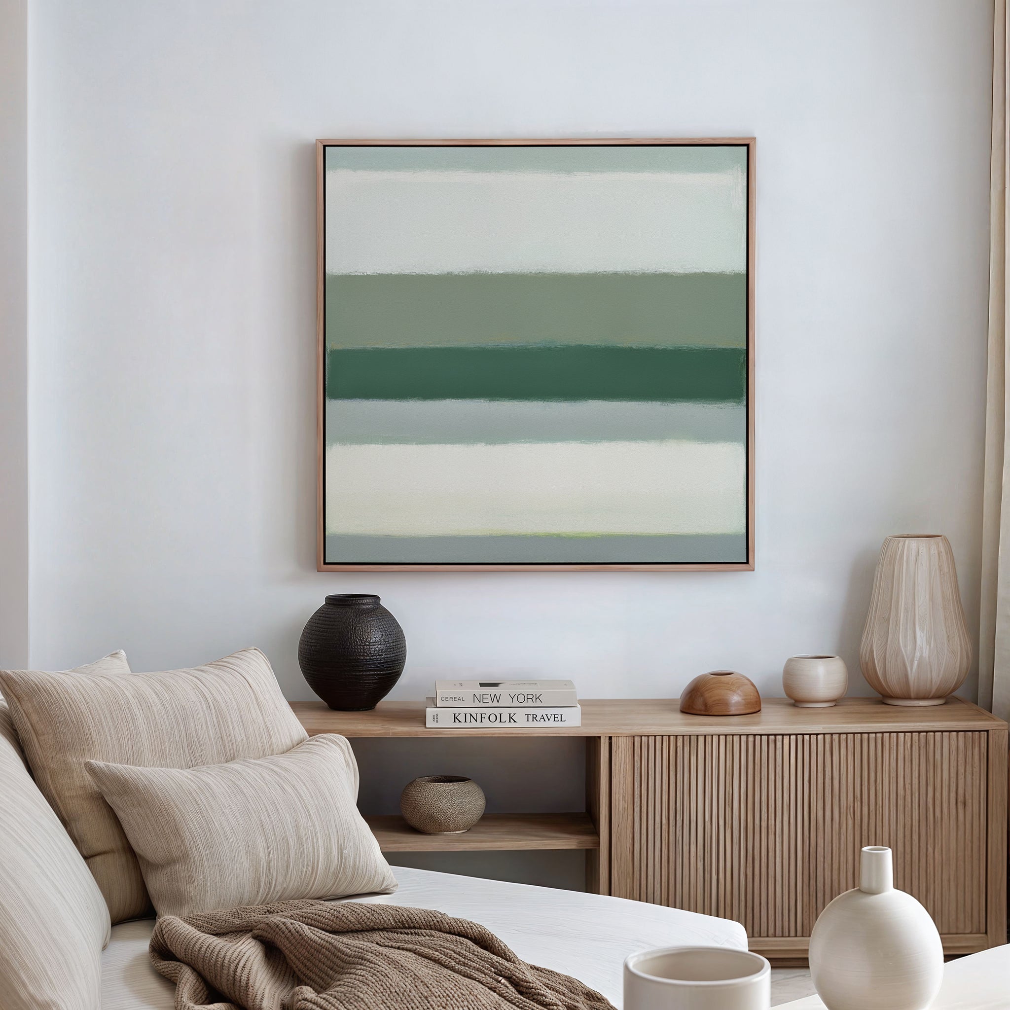 A neutral-toned living room with a beige sofa, textured cushions, a wooden sideboard, decorative vases, books, and the Sage Gradient Canvas Art - Square featuring green and white horizontal stripes on the wall.