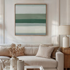 A modern living room features a beige sofa, neutral pillows, and a wooden side table with a white lamp and dried flowers. The wall is adorned with the Sage Gradient Canvas Art - Square, displaying calming green and blue stripes for serene ambiance.