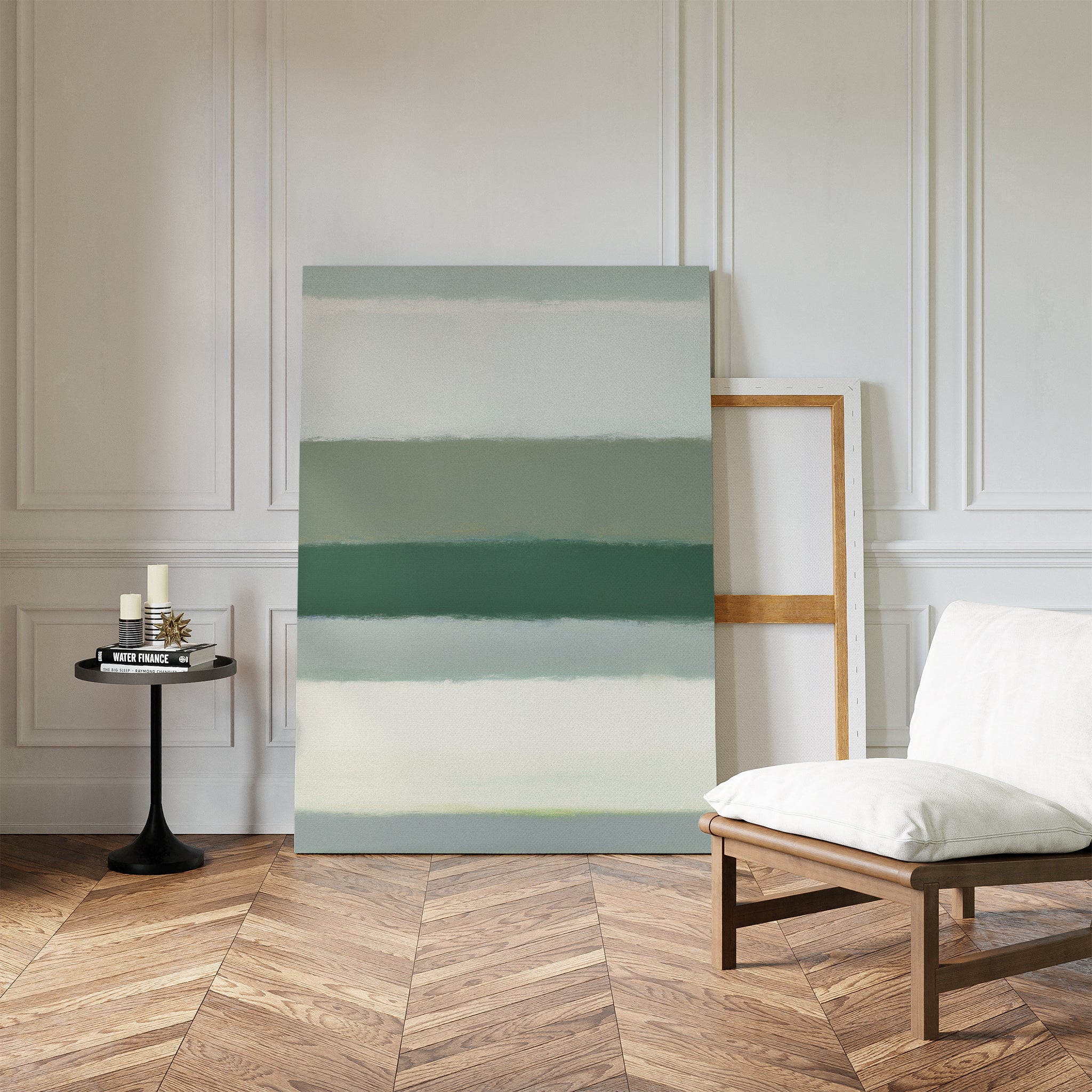 A minimalist room with chevron wood floors, white paneled walls, a cushioned chair, a round black side table with candles, and the Sage Gradient Canvas Art - Vertical in calming green tones leaning against the wall.