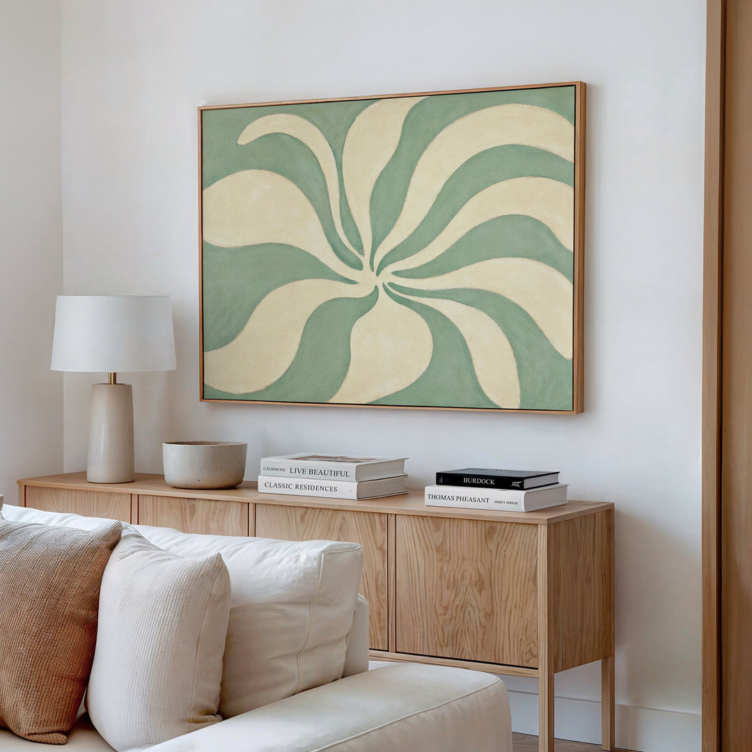 A modern living room with a light wood console table, white lamp, bowl, books, and the Sage Meditation Canvas Art - Horizontal featuring swirling sage green wall art hanging above.