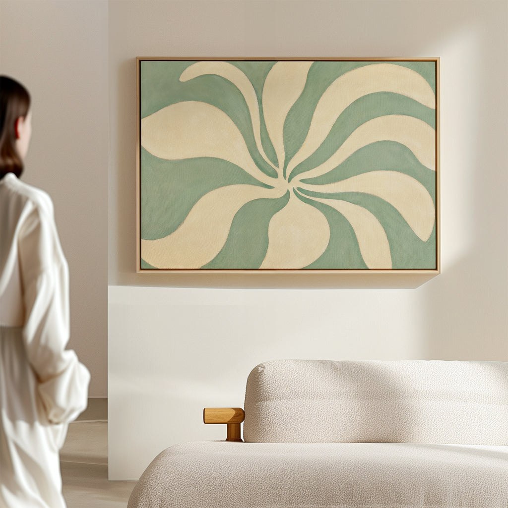 A person stands in a modern minimal room with a beige sofa, admiring the Sage Meditation Canvas Art - Horizontal, a large wall art print featuring swirling cream and green shapes.