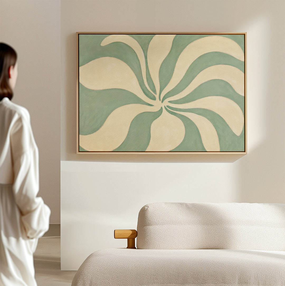 A person stands in a modern minimal room with a beige sofa, admiring the Sage Meditation Canvas Art - Horizontal, a large wall art print featuring swirling cream and green shapes.