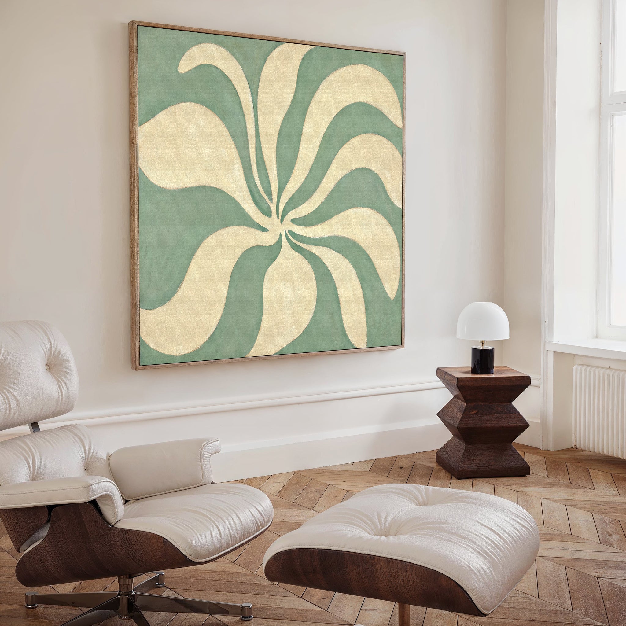 A modern living room features a white lounge chair and ottoman, a wooden side table with a white lamp, and the Sage Meditation Canvas Art - Square with abstract wavy shapes. Herringbone wood floors and natural light complete the serene look.