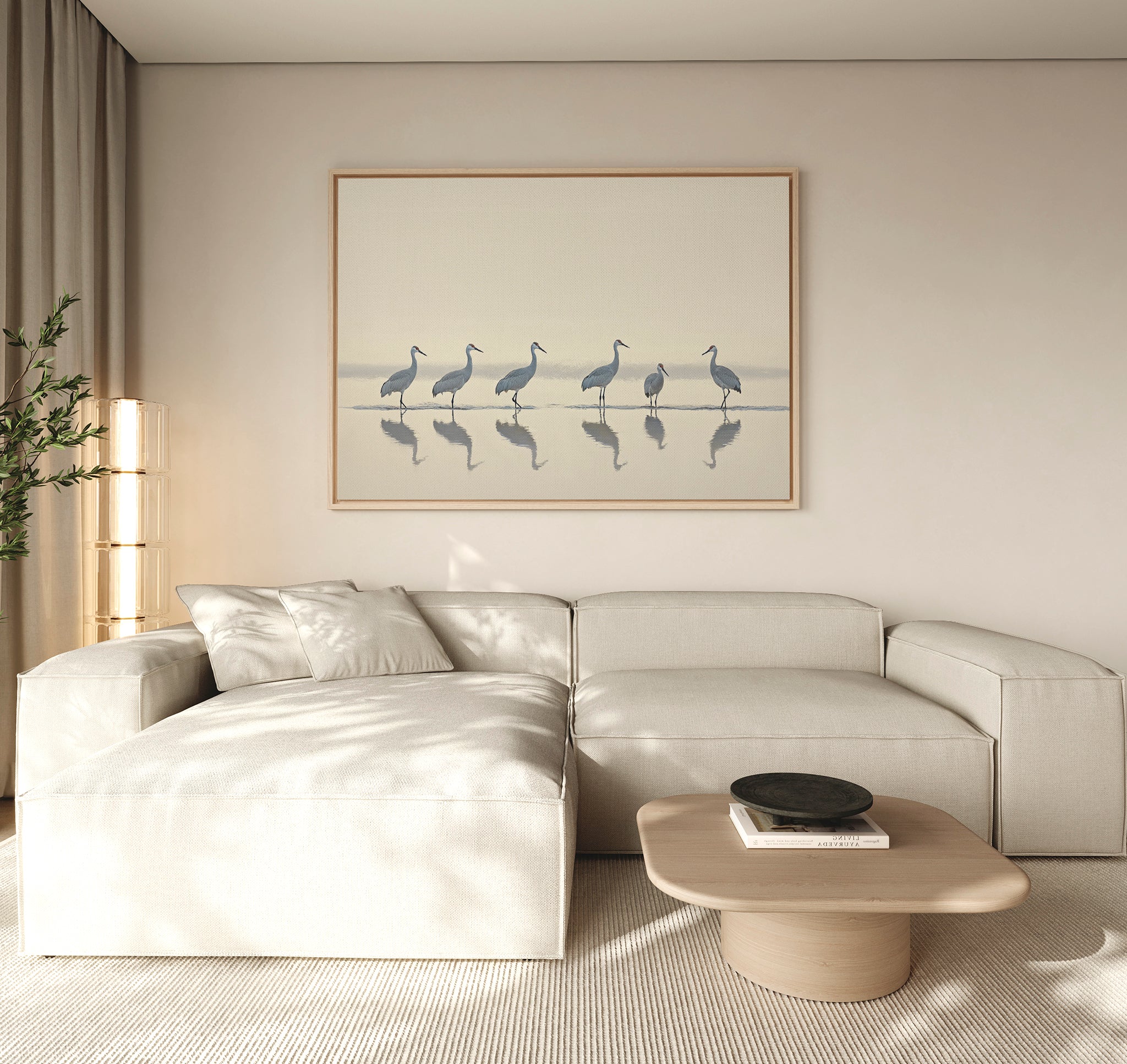 A modern living room with neutral tones, a beige sectional sofa, wooden coffee table, potted plant, and the Sandhill Procession Canvas Art - Horizontal featuring elegant cranes in water. Soft natural light creates a tranquil ambiance.