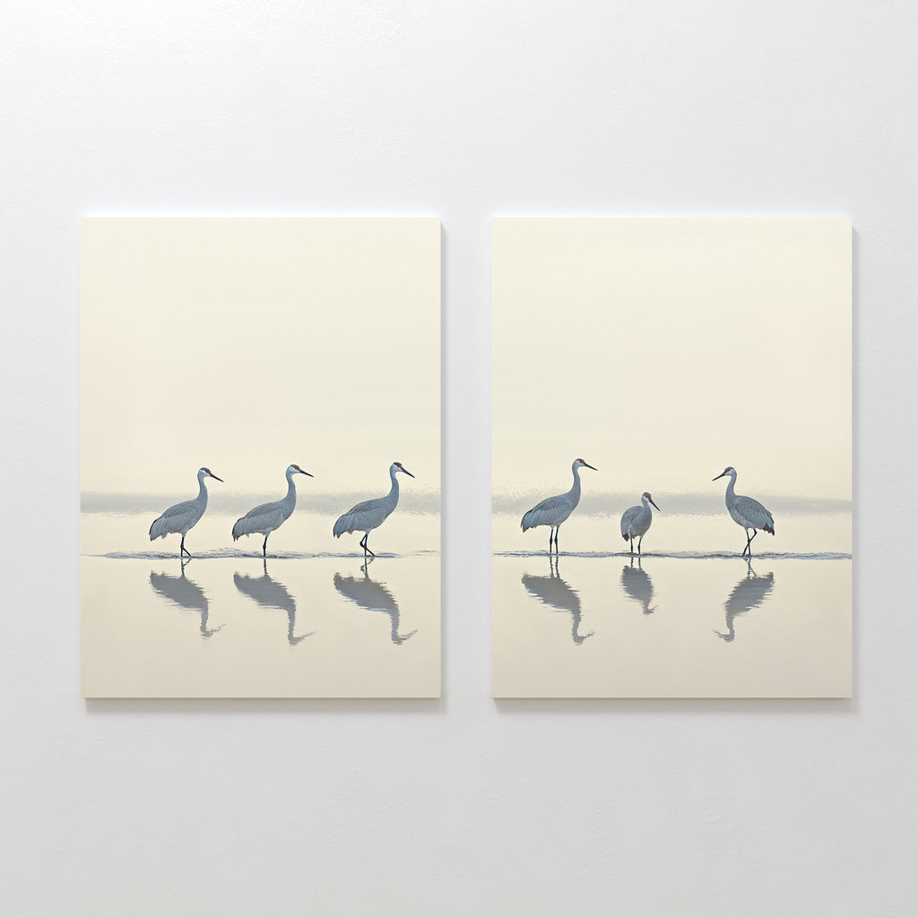 The "Sandhill Procession - Set Of 2" features minimalist paintings of wading cranes in soft, neutral tones with their reflections, set against a light background—ideal artwork for serene home decor.