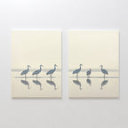 The "Sandhill Procession - Set Of 2" features minimalist paintings of wading cranes in soft, neutral tones with their reflections, set against a light background—ideal artwork for serene home decor.