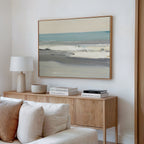 A modern living room features a wooden sideboard with stacked books, a white table lamp, a ceramic bowl, and the Sandy Retreat Canvas Art - Horizontal hanging above a beige sofa on a white wall.