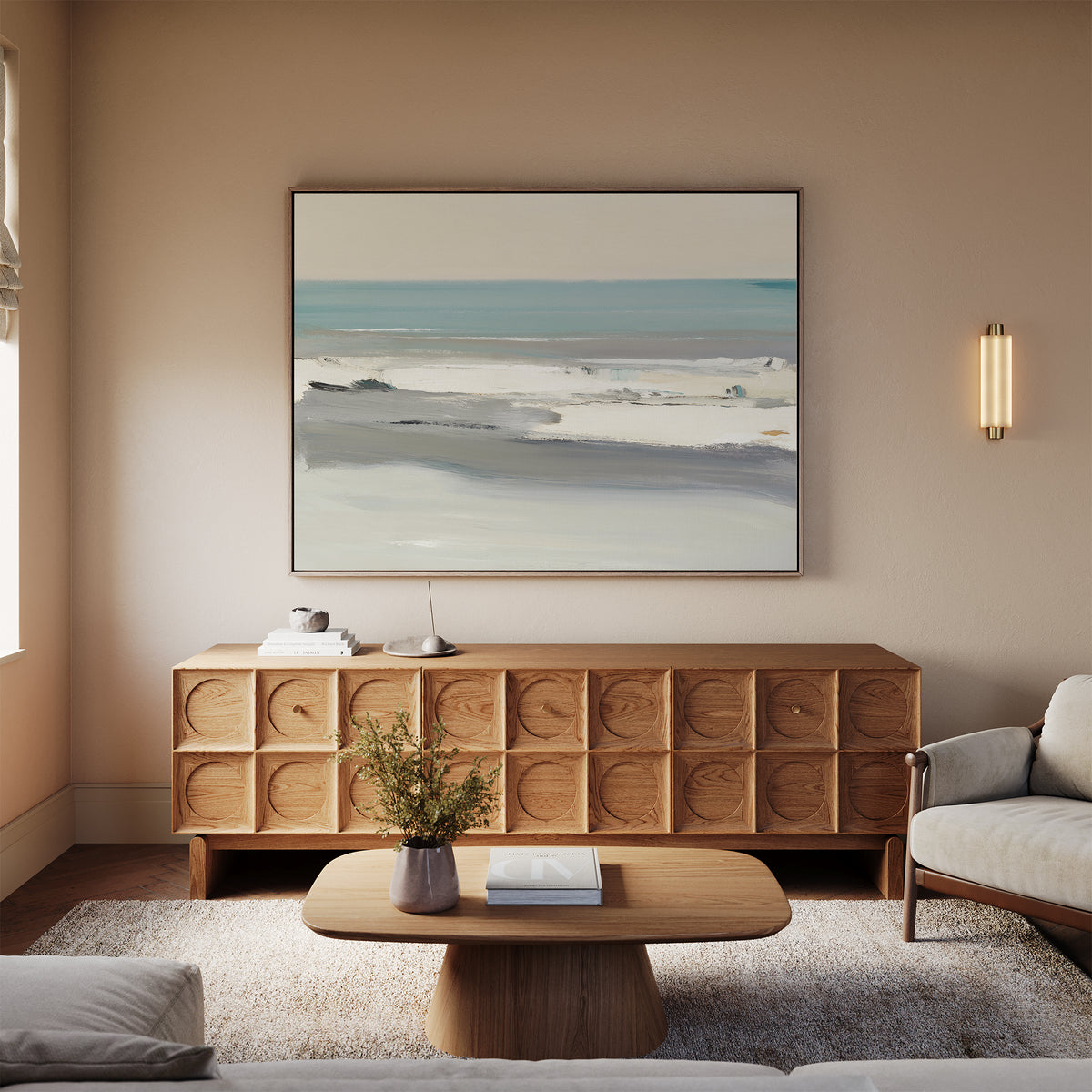 A modern living room with a light wood coffee table, textured wooden sideboard, beige sofas, the Sandy Retreat Canvas Art - Horizontal on the wall, and a small vase with flowers on the coffee table.