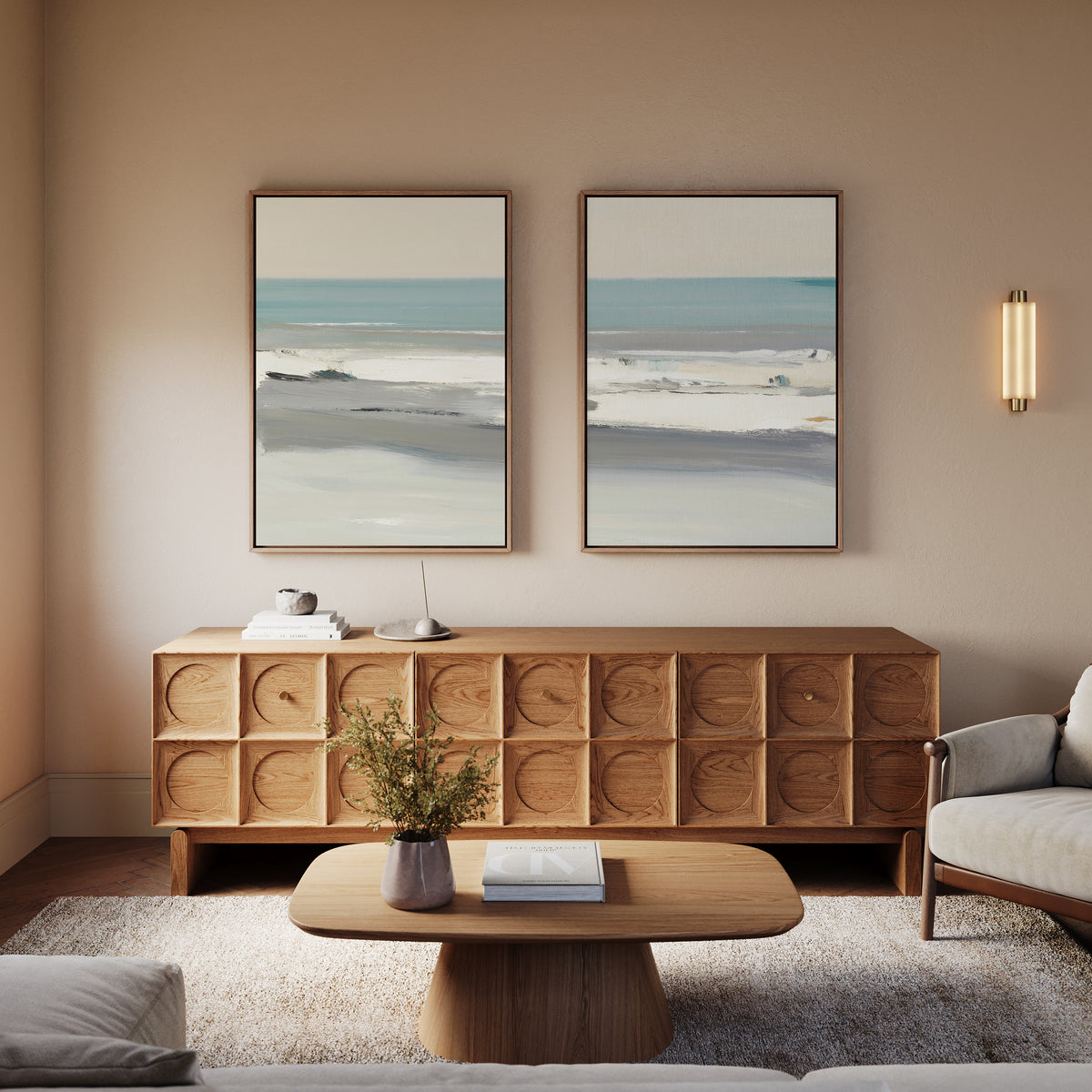 A modern living room with a wooden sideboard, coffee table, and neutral-toned sofa. The Sandy Retreat - Set Of 2 beachscape artworks hang above the sideboard, adding seaside vibes to this calm space where a small plant sits on the table.