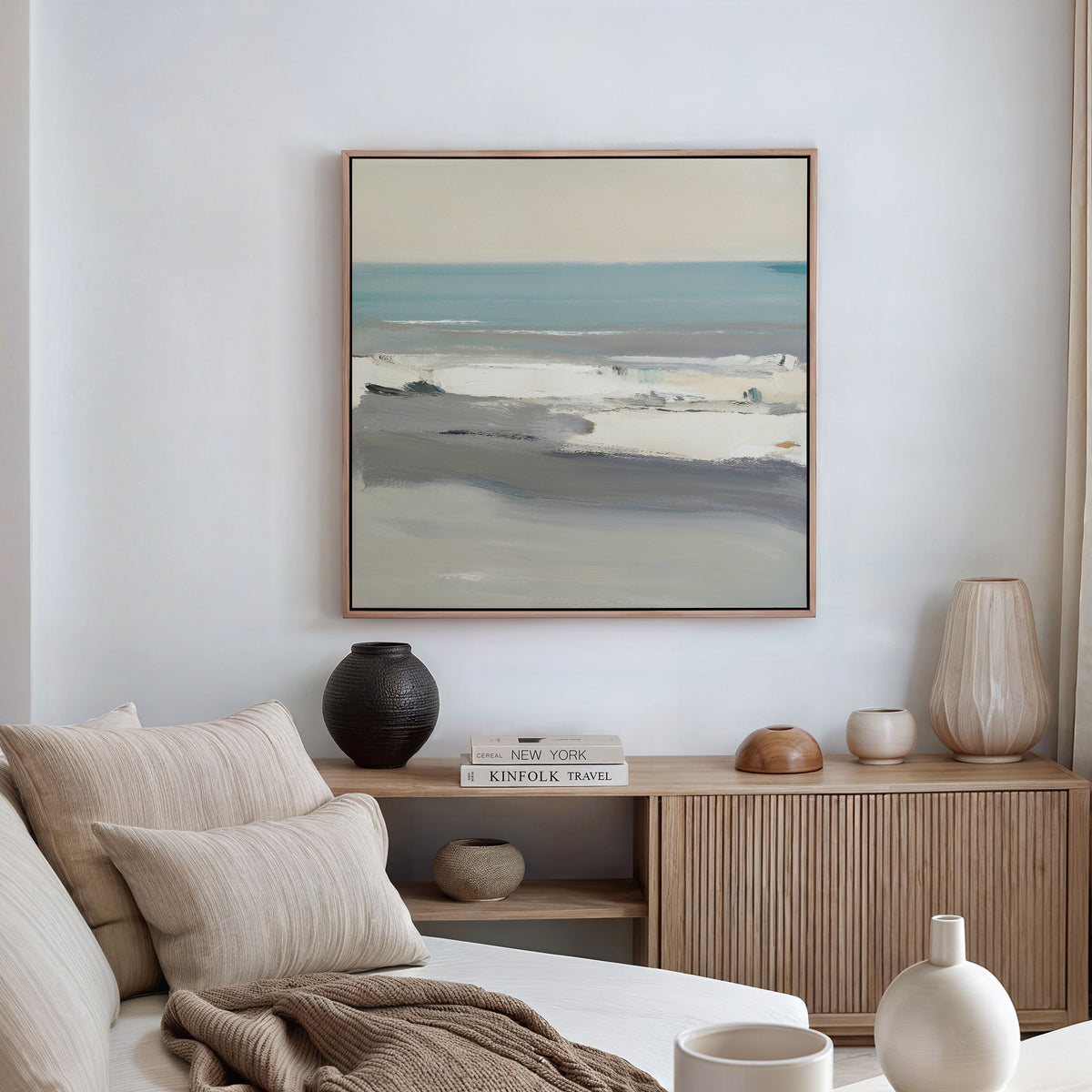 Minimalist living room with a beige sofa, neutral pillows, and a wooden sideboard topped with vases and books. The Sandy Retreat Canvas Art - Square hangs above, bringing subtle coastal vibes under soft, natural light.