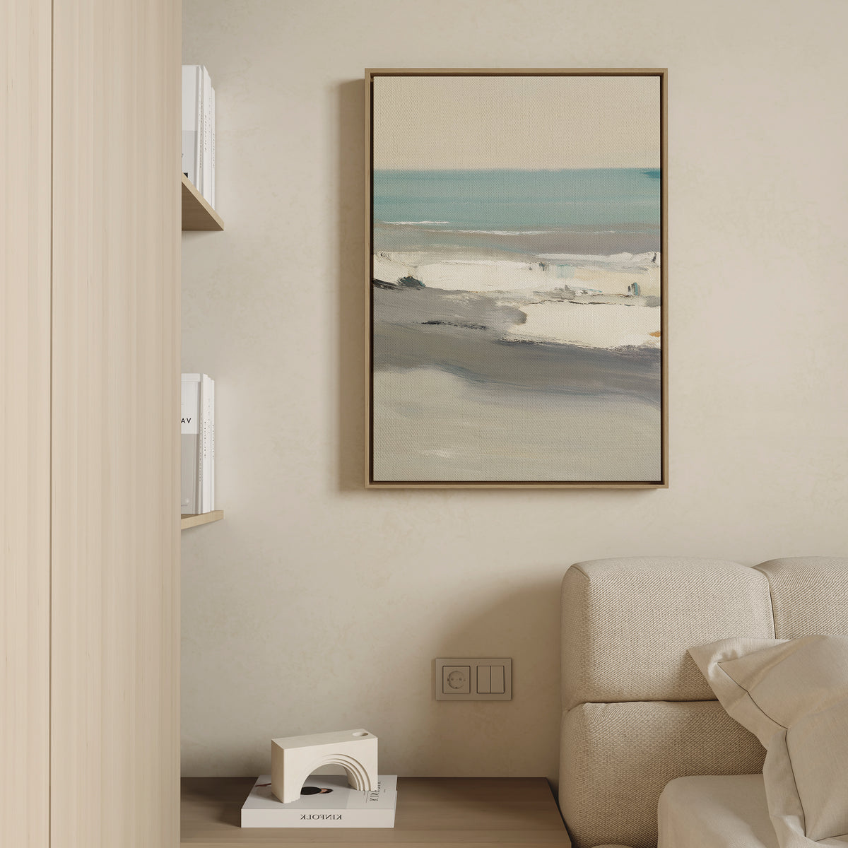 A modern living room features a beige sofa and light wooden shelves with books, while the Sandy Retreat Canvas Art - Vertical hangs above an outlet and bookend, bringing subtle seaside vibes to the cream-colored wall.
