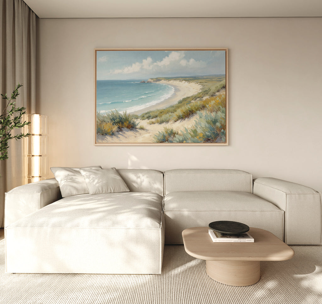 A modern living room with a beige sectional sofa, a light wood coffee table, and the Sandy Shores Canvas Art - Horizontal displayed above the couch. Natural light from a window creates a calm, airy atmosphere.