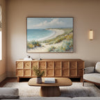 A cozy living room with neutral tones features a wooden sideboard, light wood coffee table, beige sofa, and striking beach wall art—a large Sandy Shores Canvas Art - Horizontal—hanging above the sideboard.