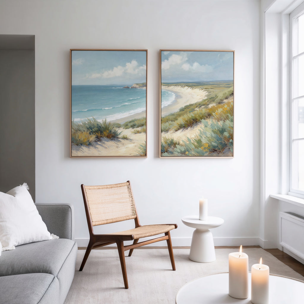 A bright living room features a modern chair, small table, lit candles, and Sandy Shores - Set of 2 large coastal canvases above the seating area, adding serene landscape decor to the crisp white wall.