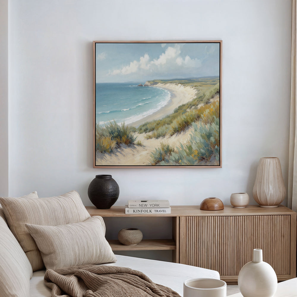 A cozy living room features a beige sofa with striped pillows, a wooden sideboard, and the Sandy Shores Canvas Art - Square above, depicting sand dunes, sea, and sky in calming coastal tones.