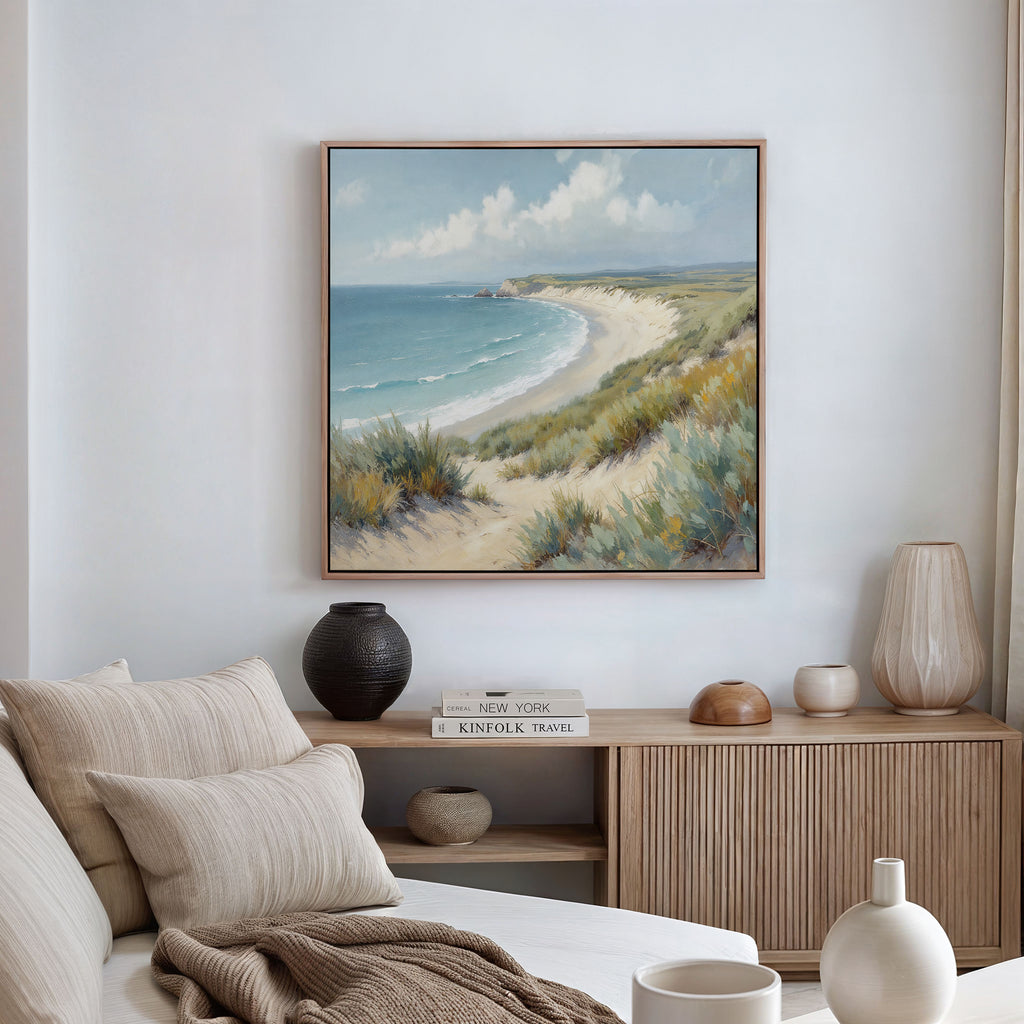 A cozy living room features a beige sofa with striped pillows, a wooden sideboard, and the Sandy Shores Canvas Art - Square above, depicting sand dunes, sea, and sky in calming coastal tones.