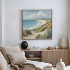 A cozy living room features a beige sofa with striped pillows, a wooden sideboard, and the Sandy Shores Canvas Art - Square above, depicting sand dunes, sea, and sky in calming coastal tones.