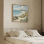 A cozy, neutral-toned bedroom showcases a large bed with white bedding and pillows, and the Sandy Shores Canvas Art - Square featuring sand dunes, grass, and ocean displayed above the headboard.