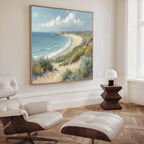 A modern living room with light wood floors, a white lounge chair and ottoman, a dark wood side table with a white lamp, and the Sandy Shores Canvas Art - Square featuring a striking coastal landscape on the wall.