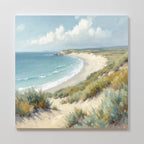 Sandy Shores Canvas Art - Square captures a sandy beach with gentle waves, grassy dunes, and a partly cloudy sky. The coastal landscape curves into the distance with green hills—ideal for adding serene beach vibes to your wall.