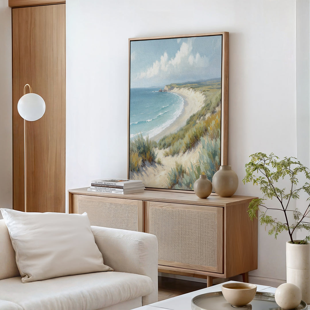 A coastal-themed living room features a light wood cabinet, beige vases, and the Sandy Shores Canvas Art - Vertical. A white sofa with a cushion and a modern globe lamp enhance the calm, airy vibe inspired by serene seaside escapes.