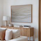 A modern living room features a light wooden sideboard with stacked books, a lamp, and neutral decor. Above, the Sandy Hues Abstract Canvas Art with soft beige and white waves brings sophisticated style to the space.