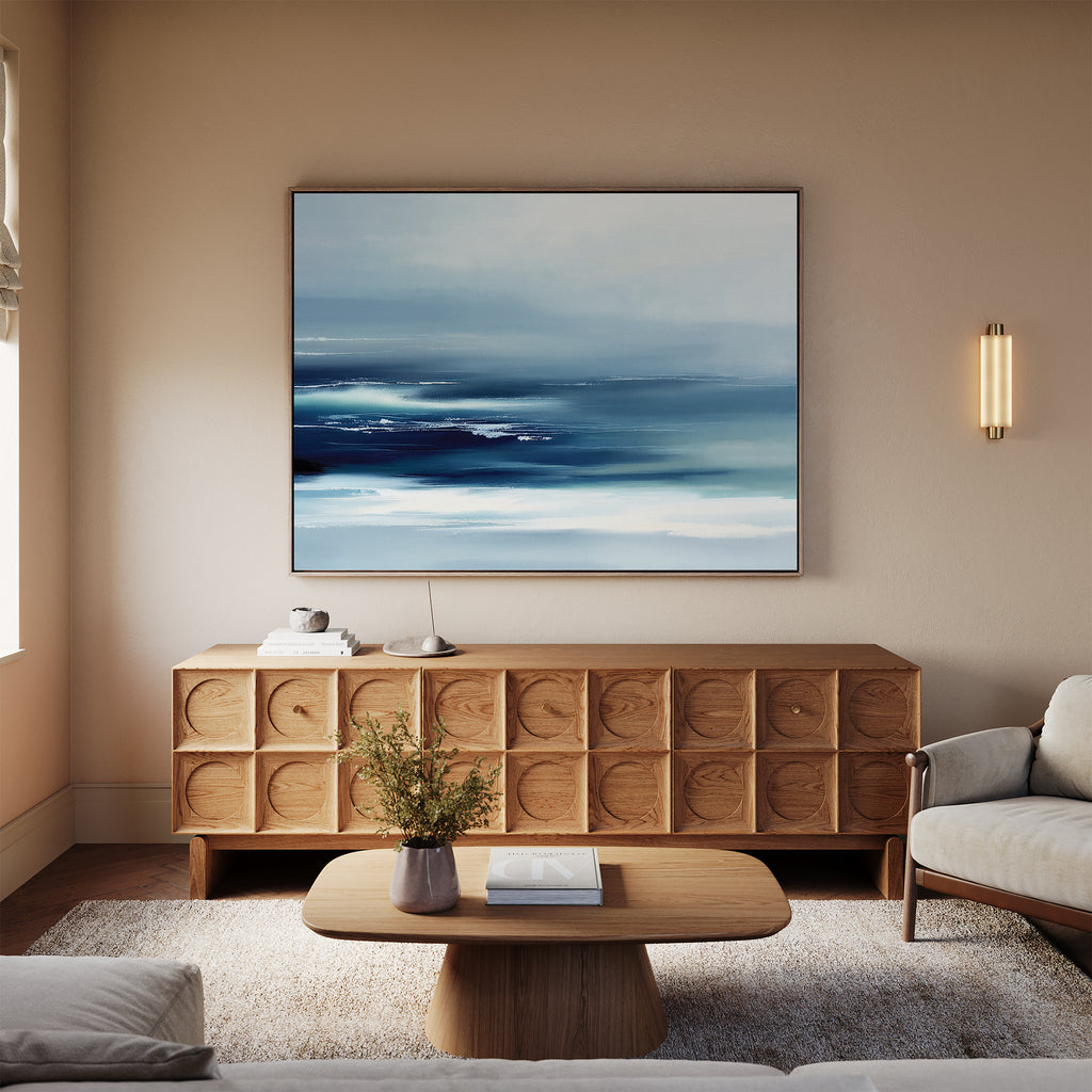 A modern living room with a light beige sofa, wooden coffee table, and sideboard, highlighted by the Sapphire Current Canvas Art - Horizontal as serene wall art. A wall sconce and flower vase finish this Nordic Park-inspired space.
